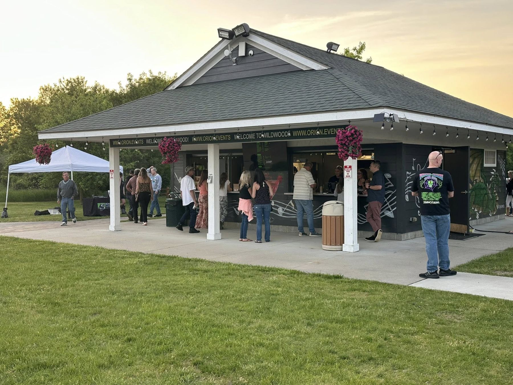 Concertgoers lined up at the AMP Pavilion Bar windows at sunset, pink petunias hanging from the porch