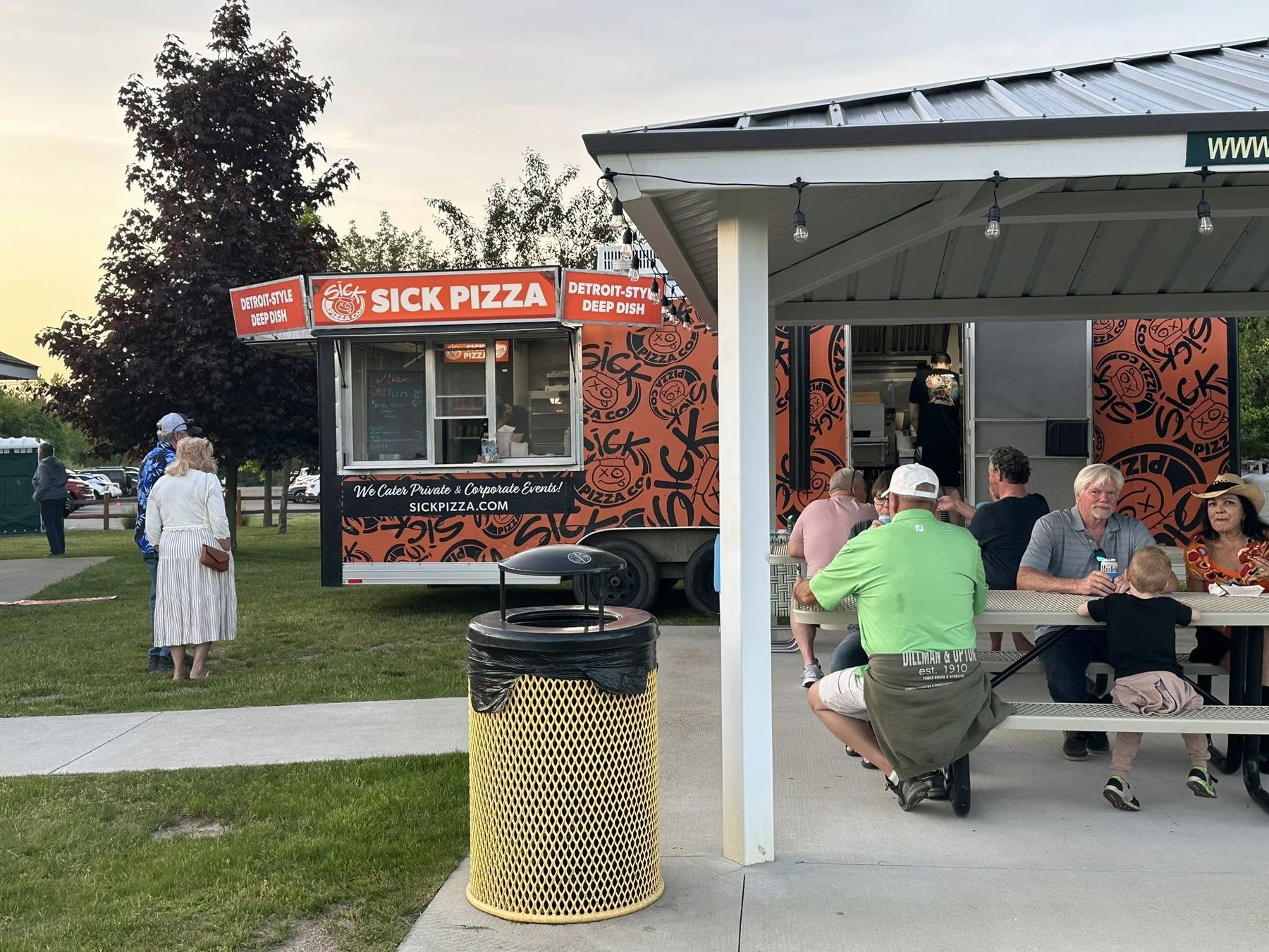 The Sick Pizza trailer beside the covered picnic pavilion, guests eating at the tables